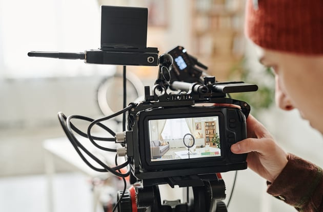 Screen of camera and hand of cameraman standing in spacious living room
