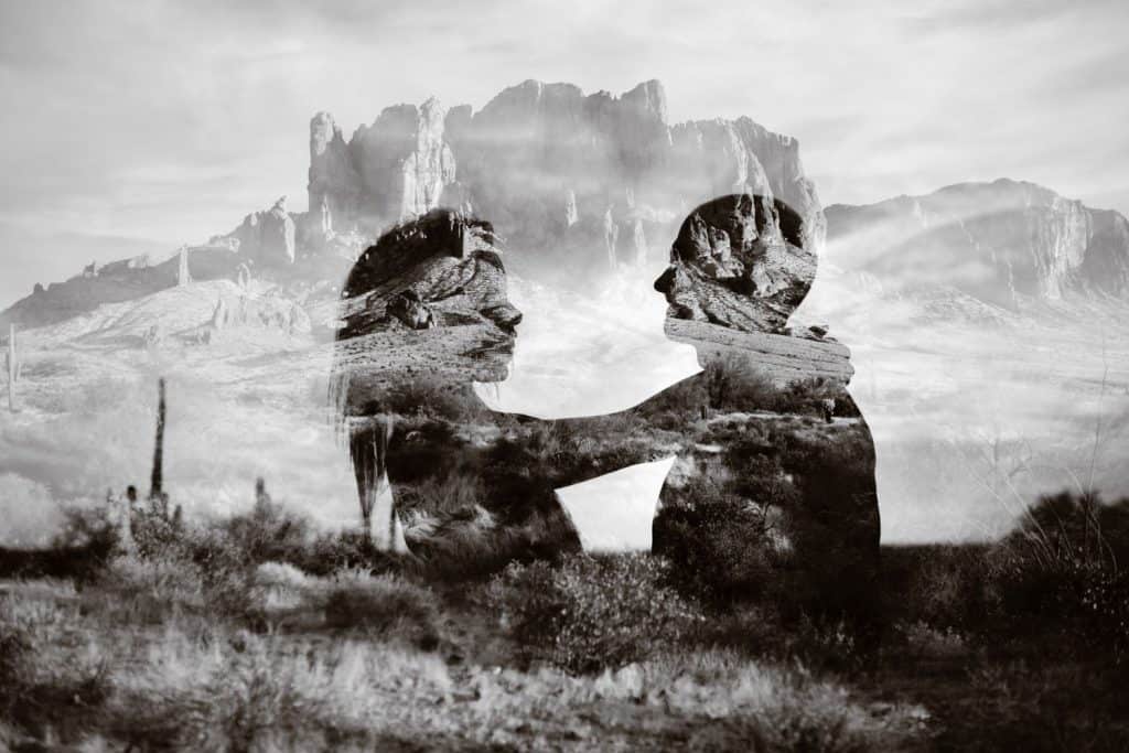 A double exposure of a couple looking at one another in front of a desert canyon