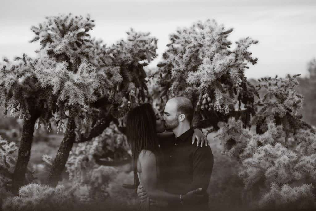 A black and white portrait of an engaged couple kissing in the desert